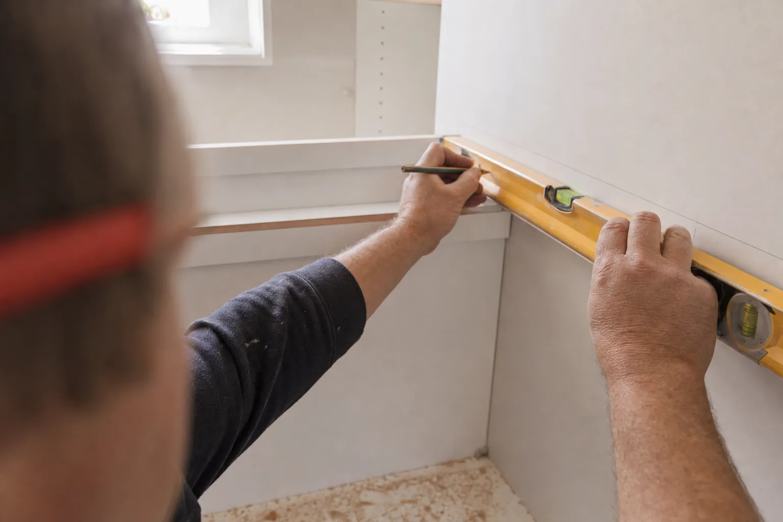 A carpenter holding a spirit level along the wall and marking the line with a pencil.